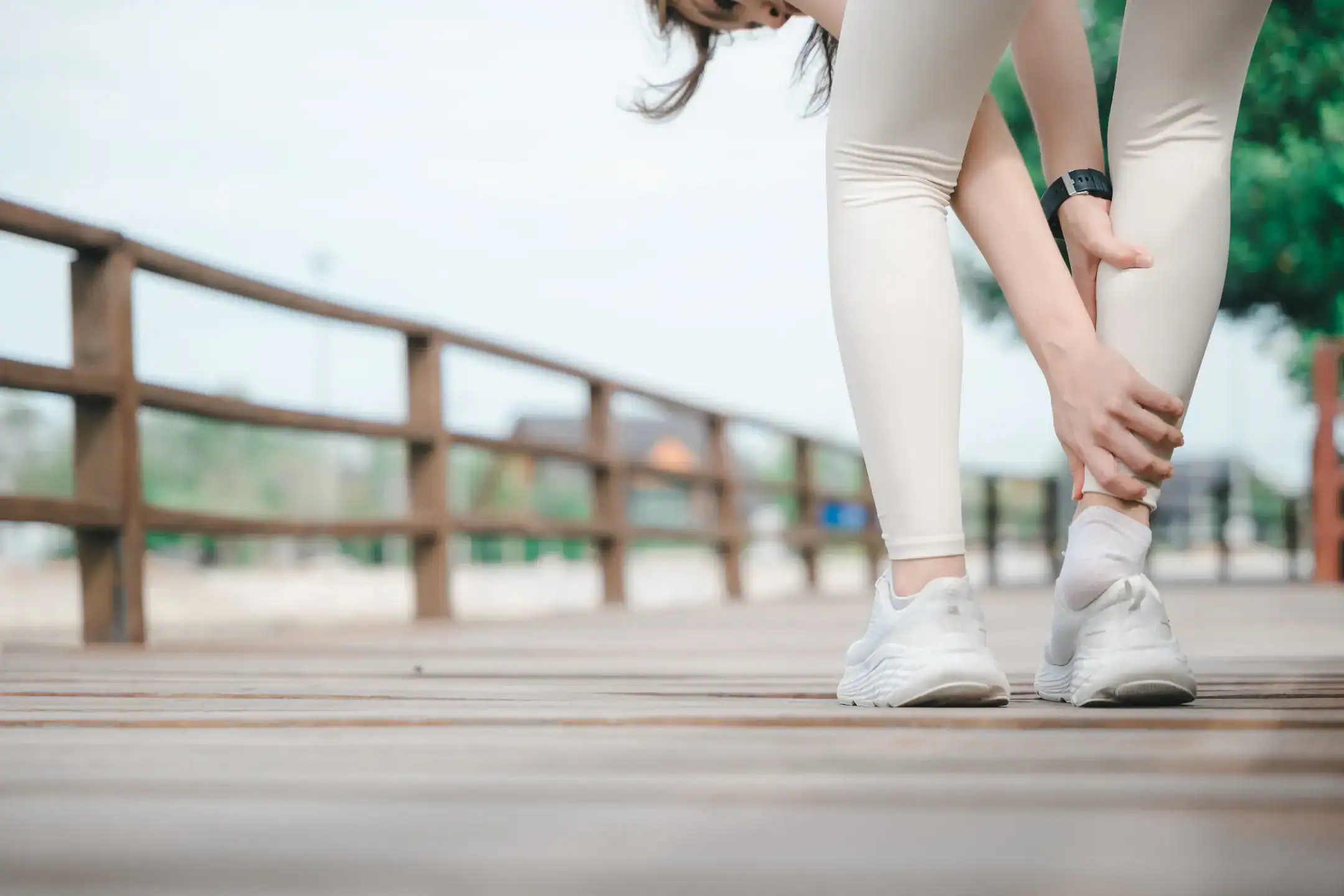 female runner with achilles tendon injury holds painful lower leg suffering from sudden calf muscle strain ankle sprain outdoor training wooden boardwalk